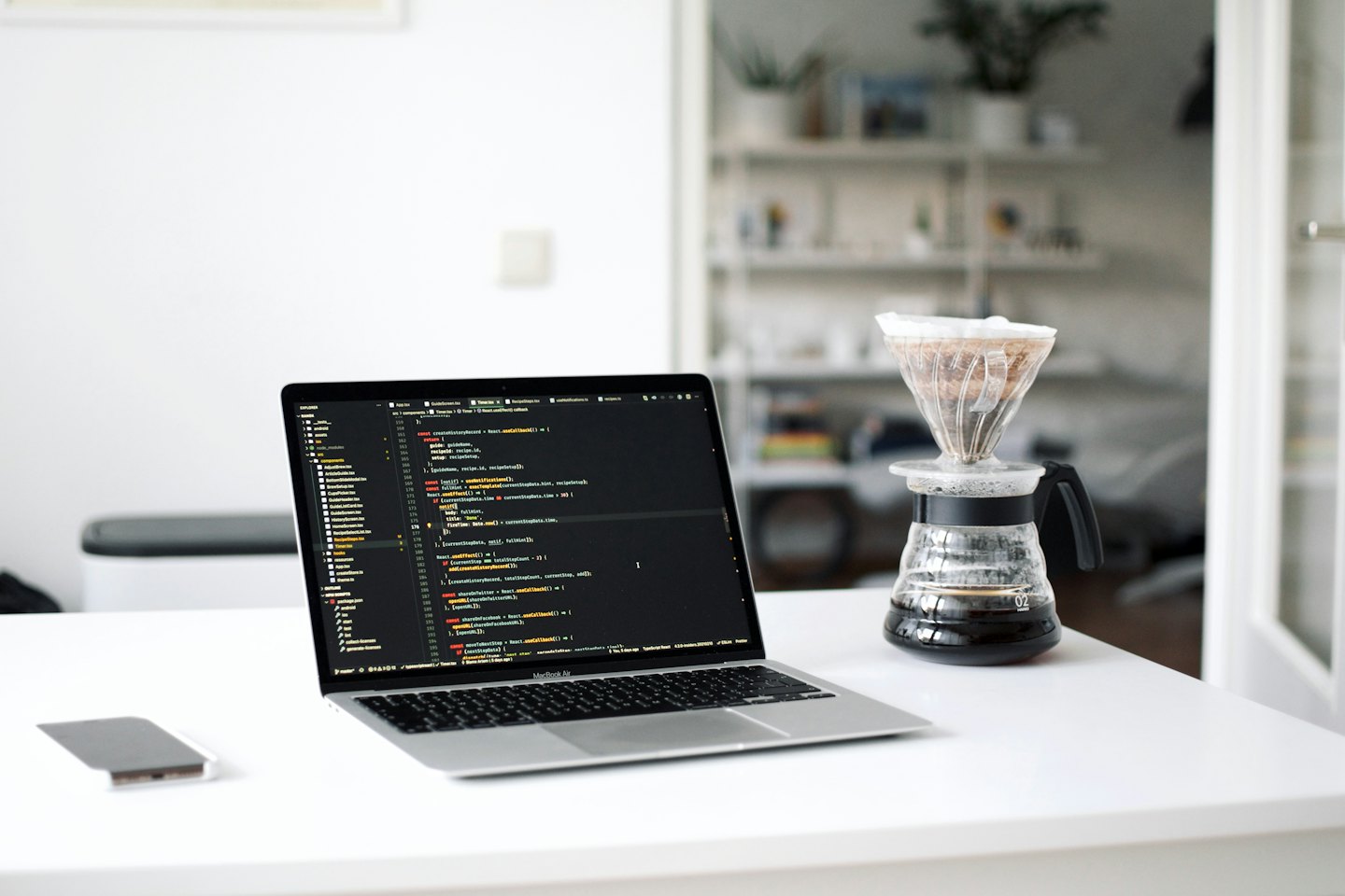 A laptop showing code sits on a desk with coffee.